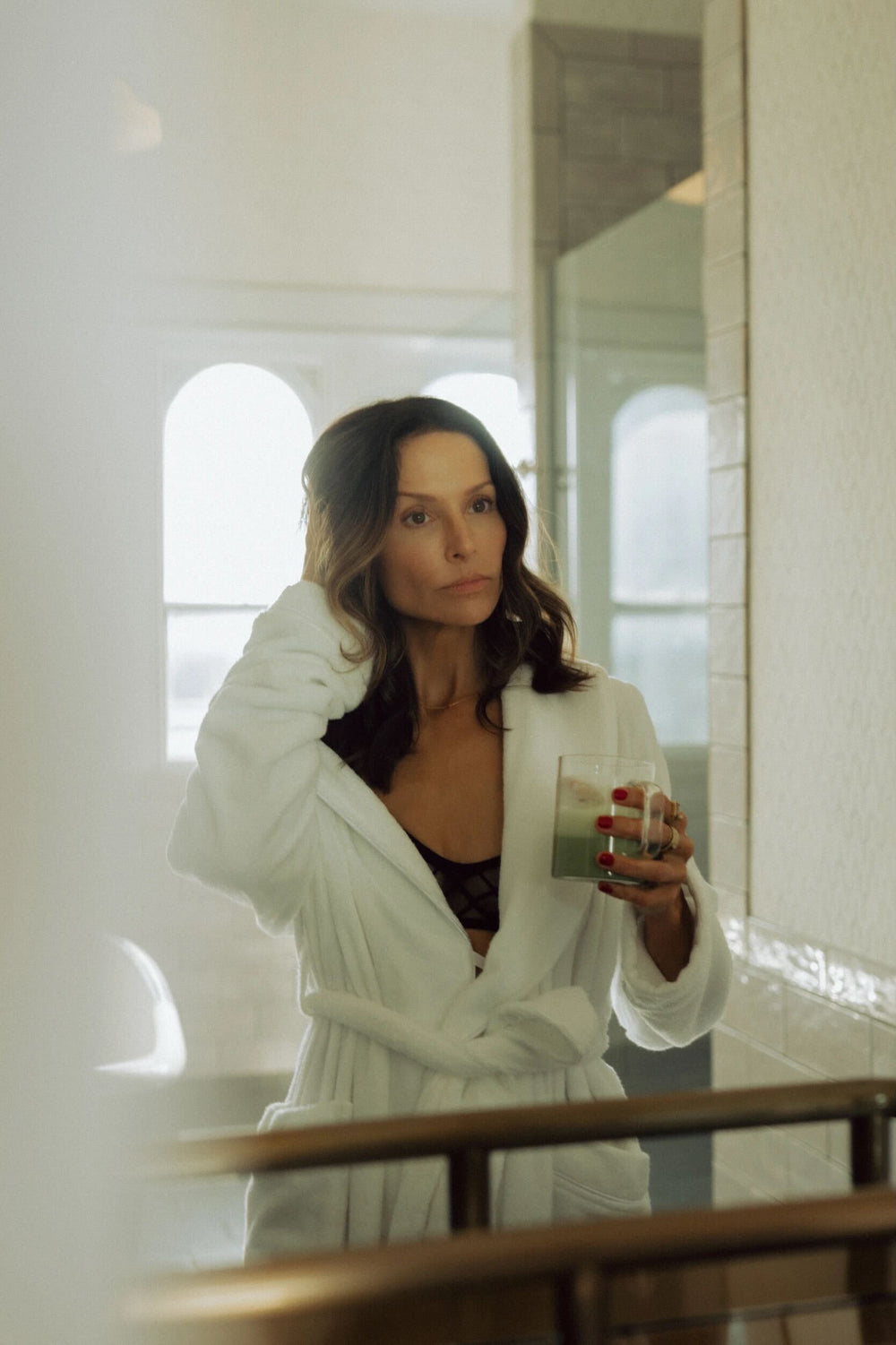 Woman in a white robe holding a glass of water in a bathroom.